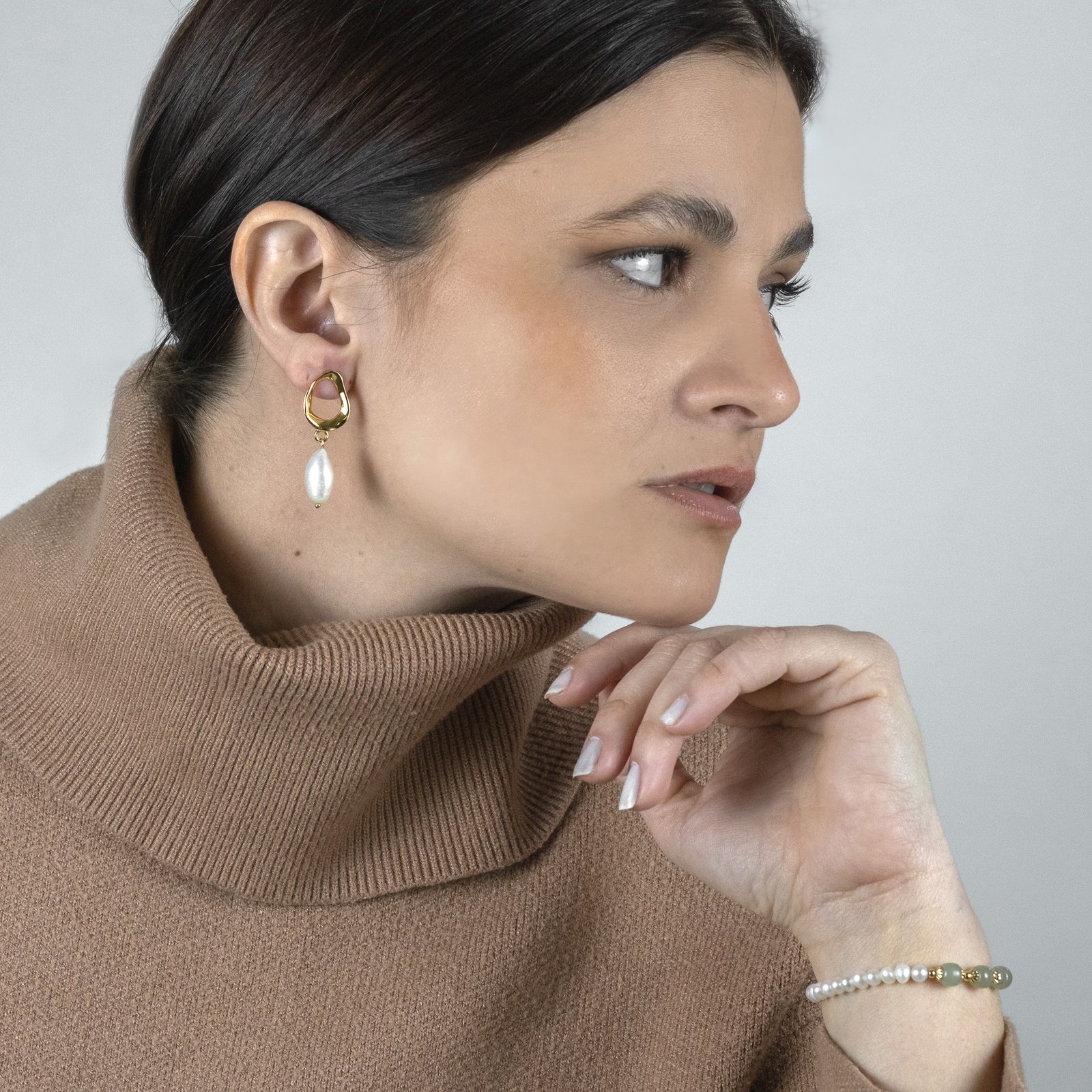 woman looking sideways showing her pearl drop earrings and bracelet